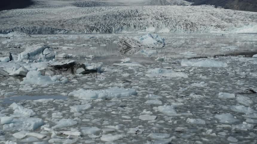 Pieces of melting ice are floating in the arctic water and there are snow covered mountains in the distance