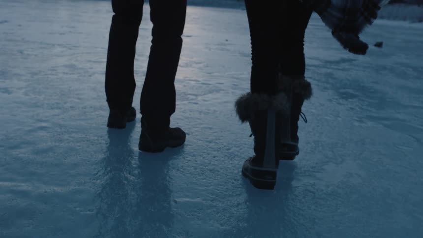 Two people walk and slide across an icy lake