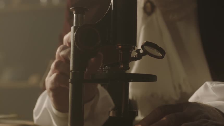 An older man's hand turns the wheel on a microscope