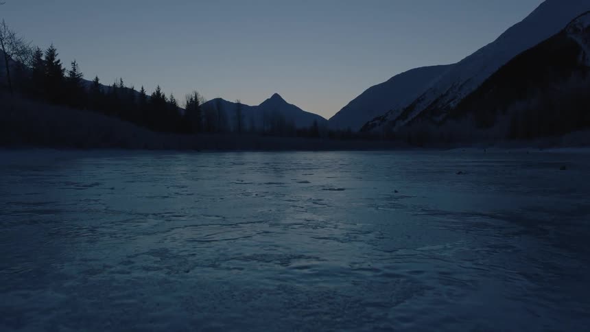 A river is frozen over before a mountain
