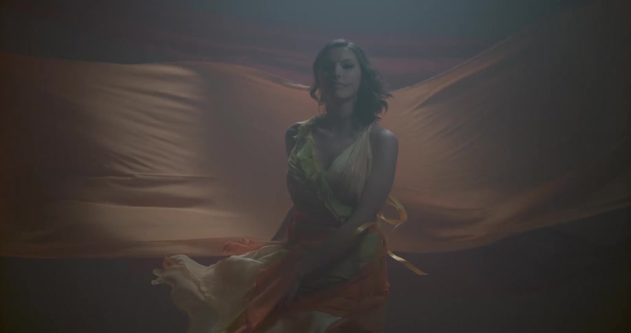 A woman in an orange dress dances near fabric