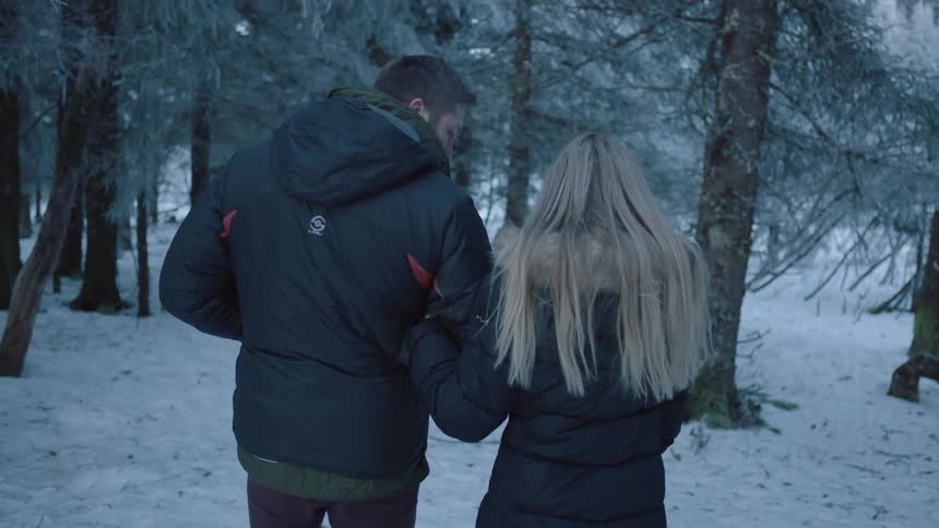A man and woman walk through a snowy forest