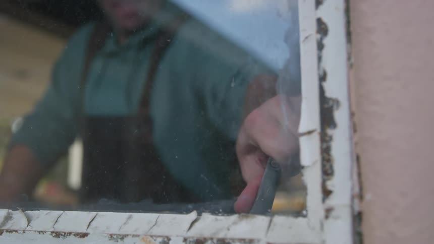 A man wearing an apron is twisting open the handle of an old window