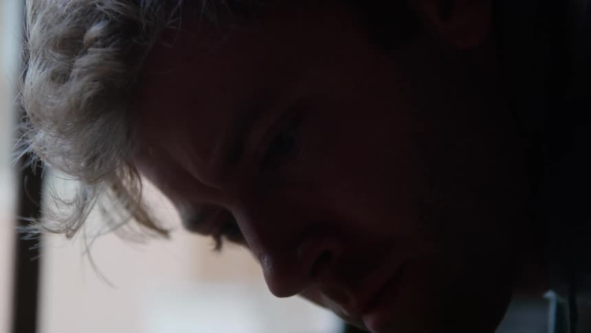Close up of the face of a blonde man turning his head near a window
