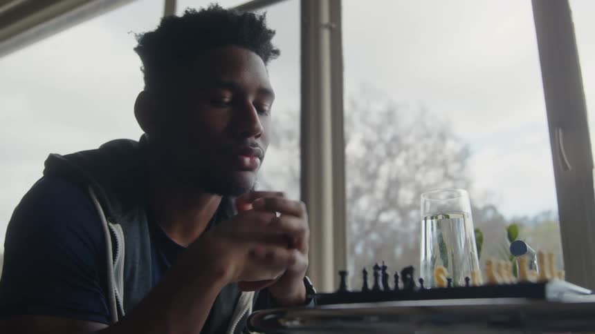 Two young men sitting at a table together indoors playing chess