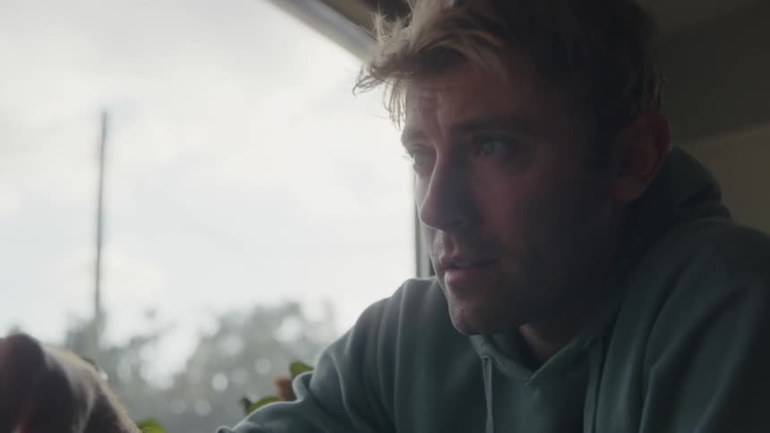 Man sits with glass of water seasoning food before looking out the window