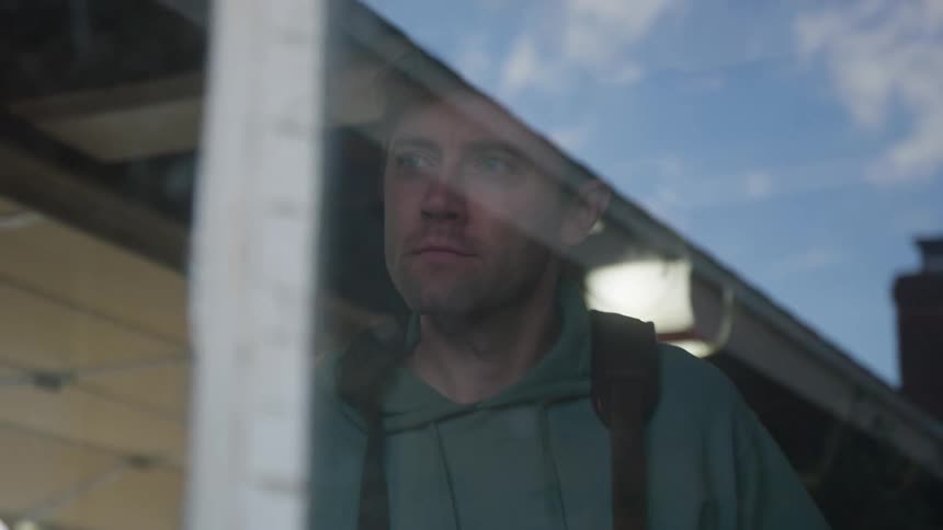 Man working on a store blows over a surface to clean it in front of a window reflecting a blue sky