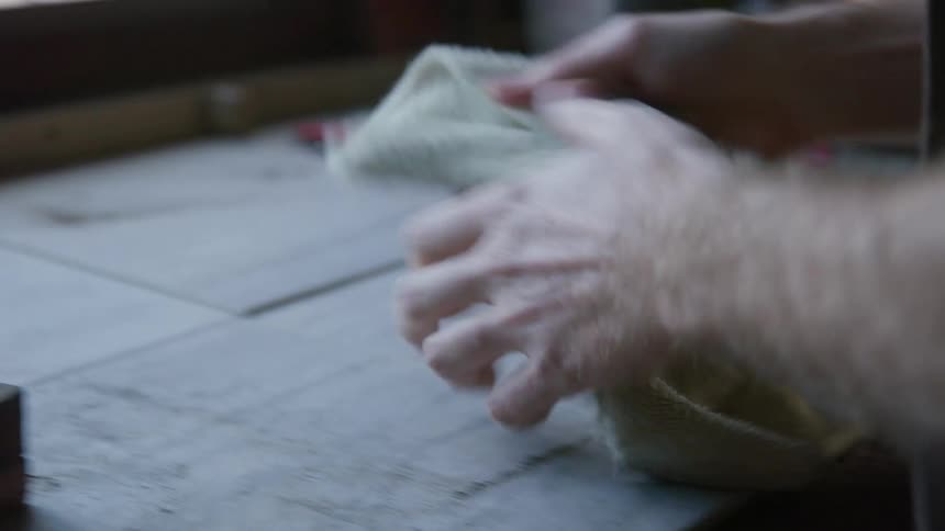 A man pulling a rag from his pocket and wiping the wood surface in front of him