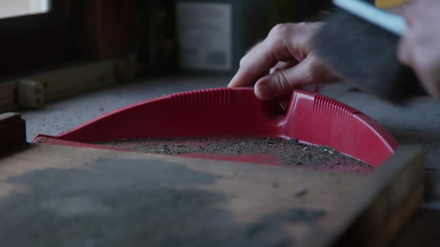 A man using a hand broom and dustpan to clean dirt from a tabletop