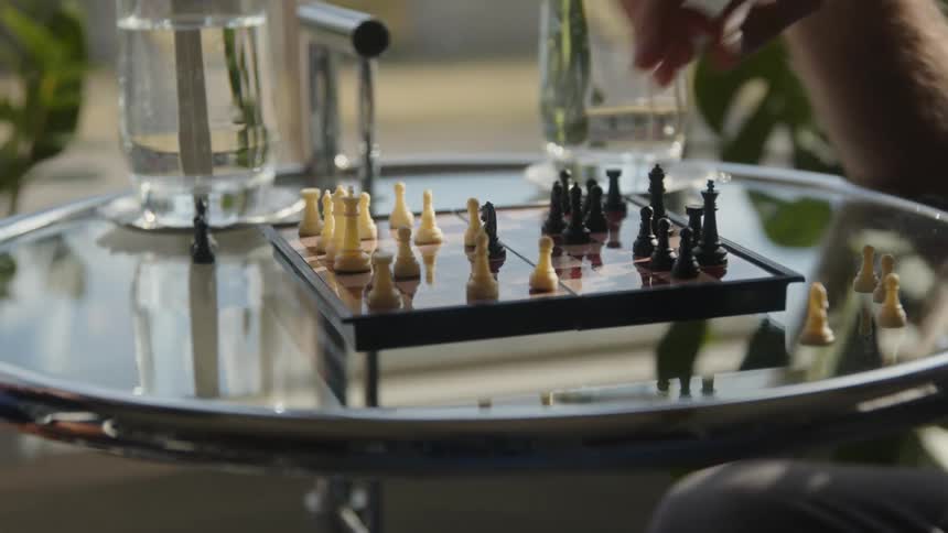 A man playing chess on a glass table moves a game piece and takes the opponents pawn