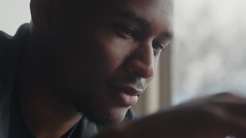 A man is smiling as he looks at the chess game and moves his piece on the board as a glass of water sits near the window