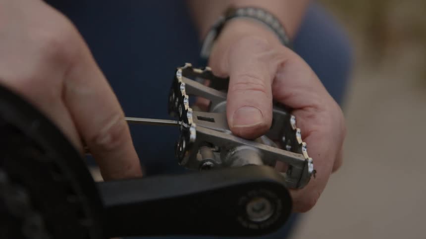 A man is using a swiss knife to turn the screw on a bicycle peddle