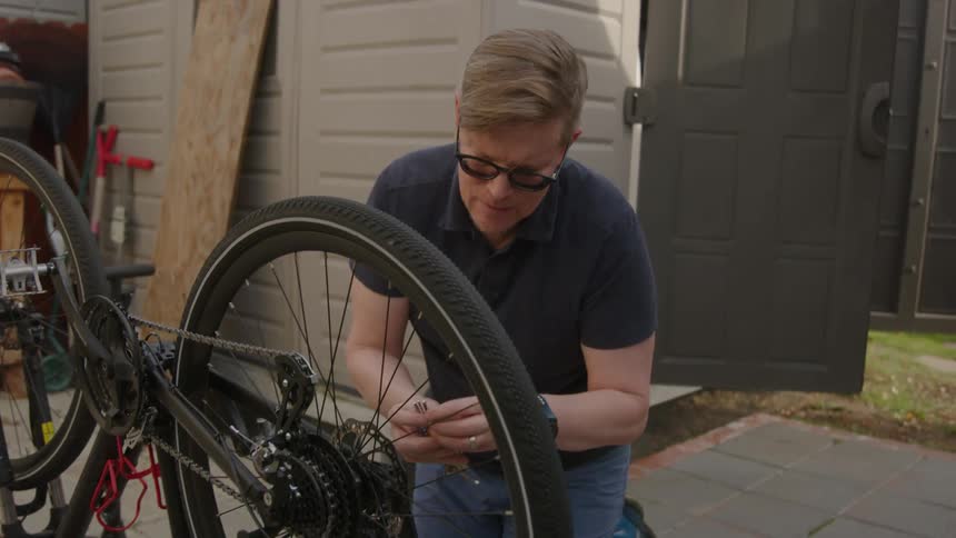 A man repairs his bicycle next to a shed