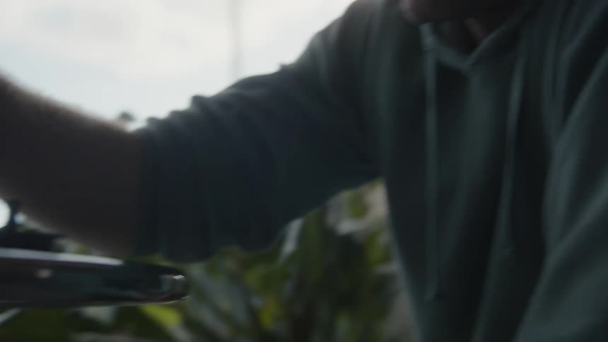 A man is sitting at a table playing chess with himself near a window as he moves the game pieces