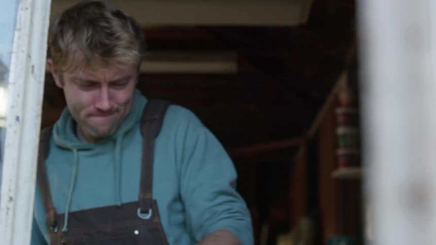 Man stands in workshop working briefly looking out the open window