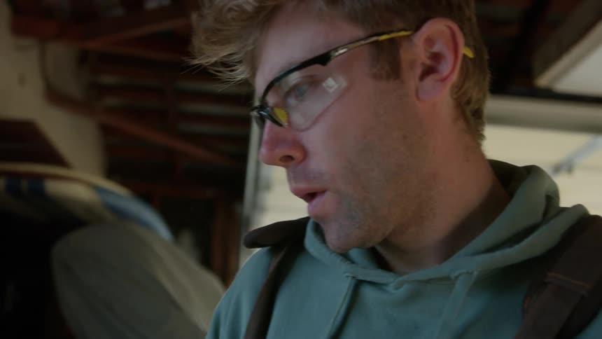 Close up of the face of a blonde man wearing protective glasses working on a garage