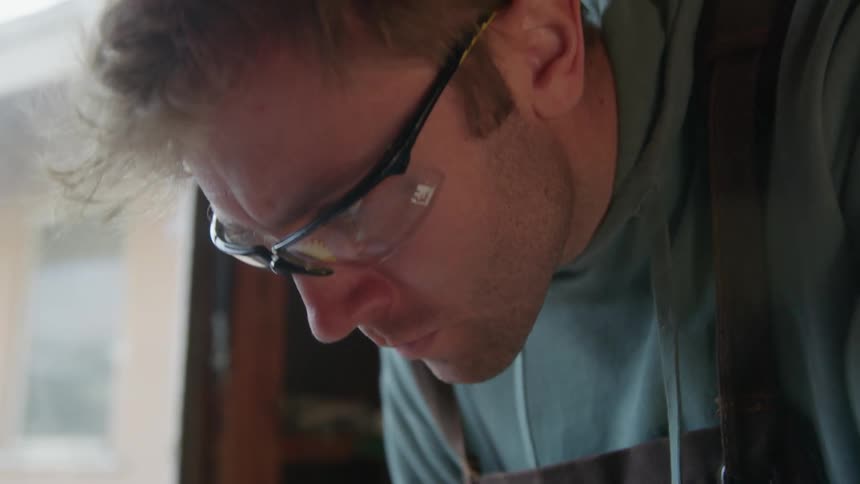 A man wearing safety glasses is looking down as he works near a window