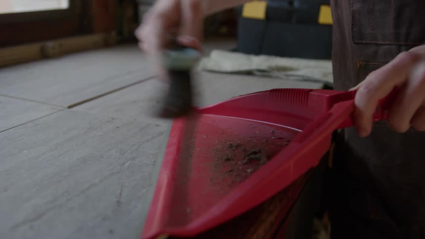 A man is standing next to a table brushing dirt into a dustpan
