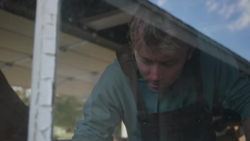Man working on a store cleans a surface in front of a window reflecting a blue sky