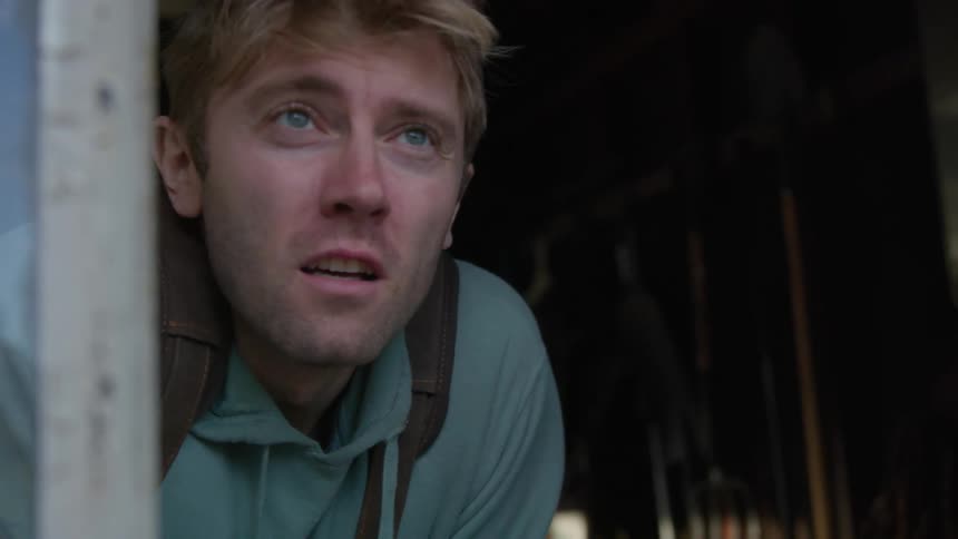 A man is standing indoors and looking out a window