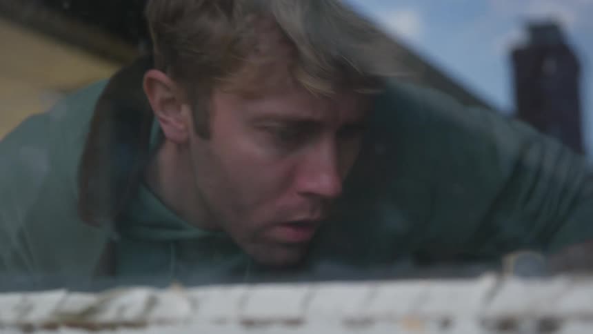 Man blows particles while working as window reflects blue of sky
