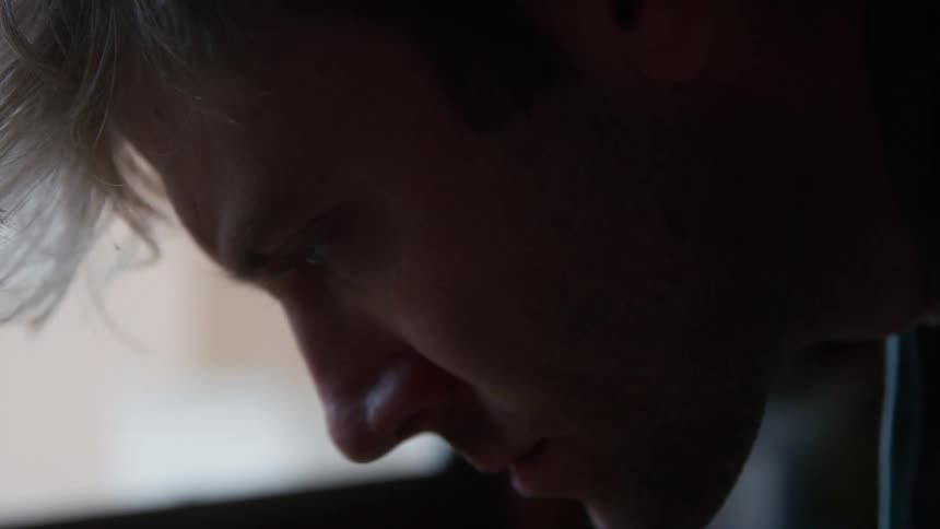 A close up of a mans face leaning forward and looking contemplatively