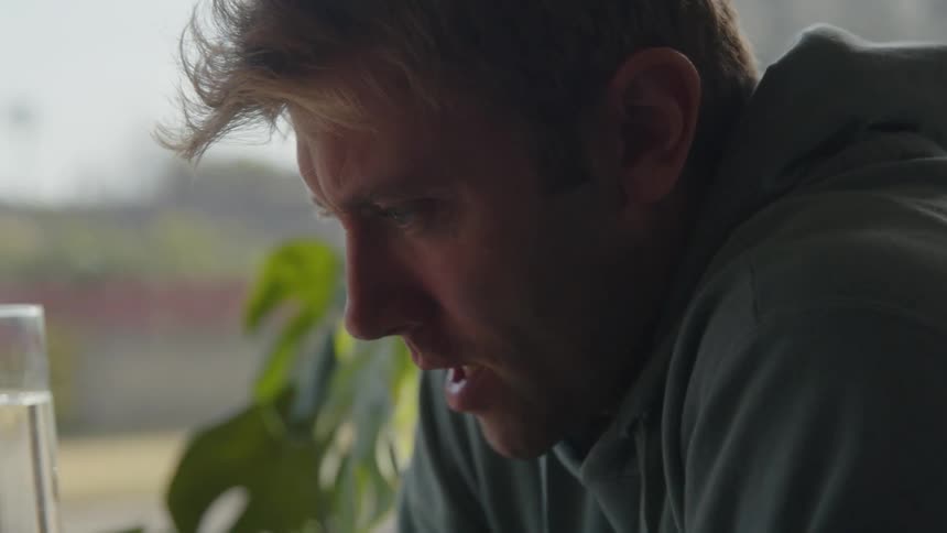Man sits near window concentrating on item on table