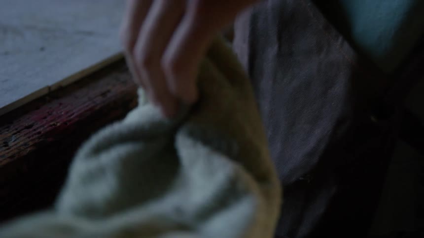 A man removes a towel from his pocket to wipe sawdust from a table
