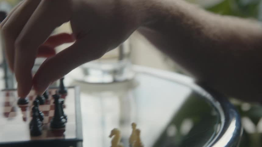 Man sits at glass table near window while playing on portable chessboard