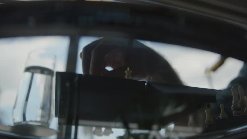 Man sits at glass table near window playing with chess pieces on chessboard