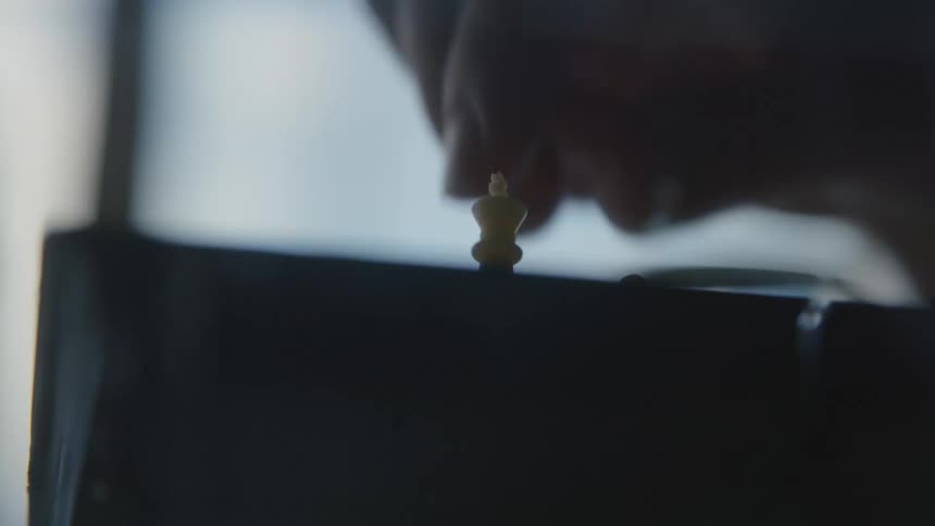 A close up of a persons fingers moving chess pieces on a board
