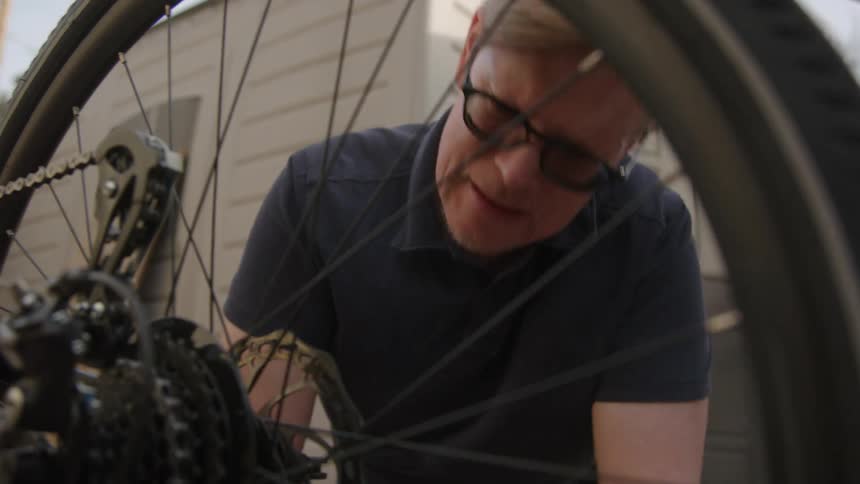 A man is outdoors and is fixing a bicycle