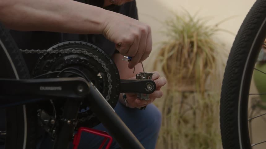 A close up of a man using a tool to adjust the pedal on his bicycle