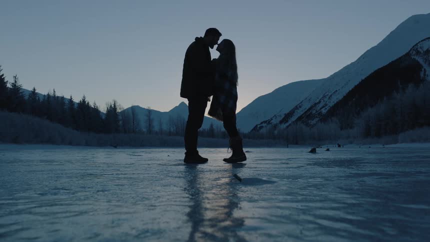 A man and a woman kiss while standing on ice covered ground