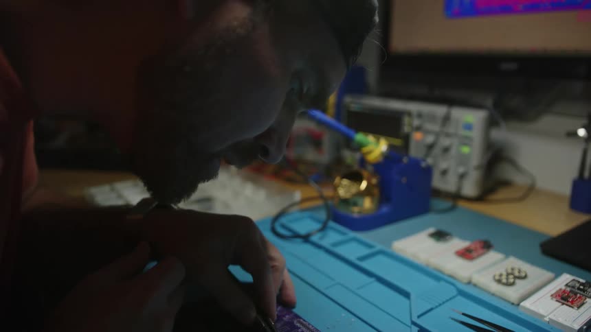 A man solders a circuit board at his desk