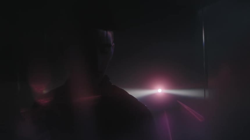 A man is standing in the dark with a projector going behind him
