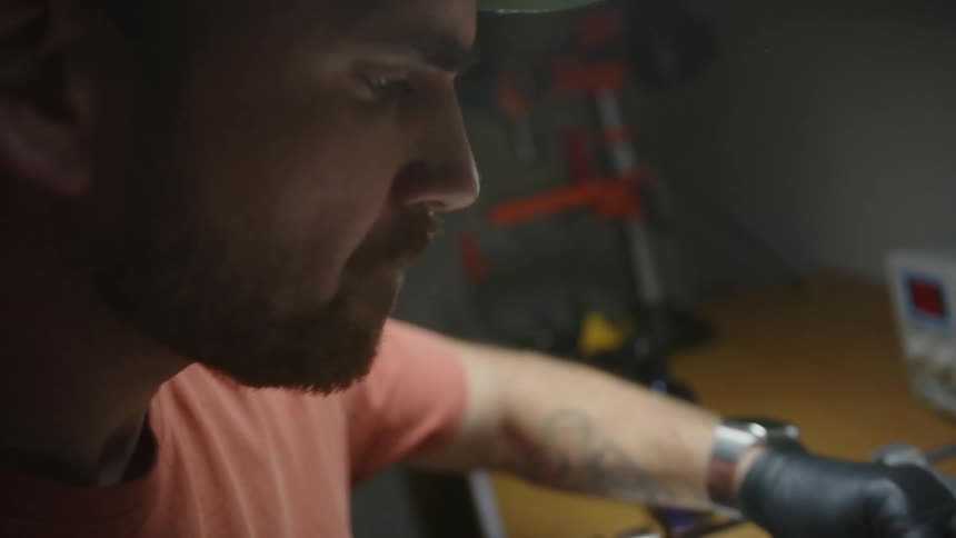 Man wears gloves while moving small item over glossy surface in workshop