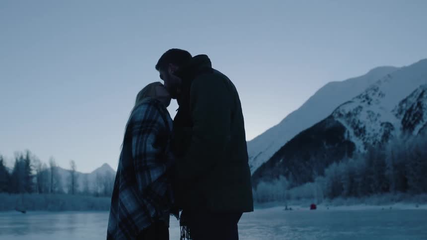 A man and woman stand on a frozen lake kissing