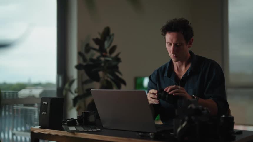 A man puts together a camera lens while sitting at his desk