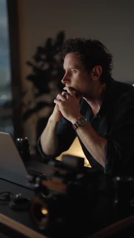 Vertical video of a man working on a laptop in his home office at night