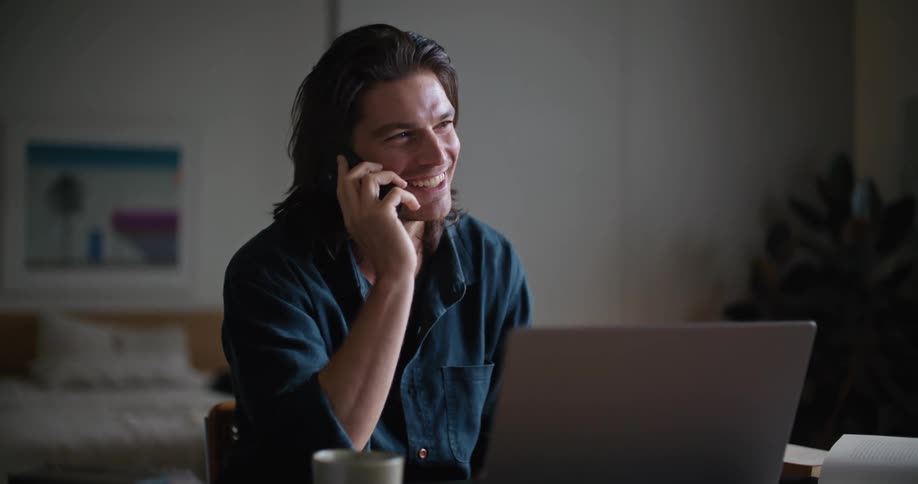 A man smiling and laughing while talking on the phone in front of a laptop