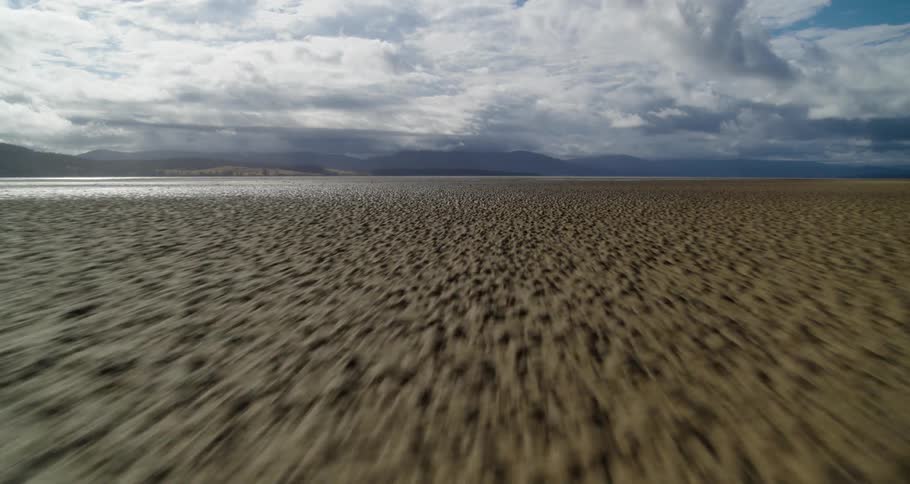 Muddy and wet land stretches to misty mountains on horizon under a cloudy sky