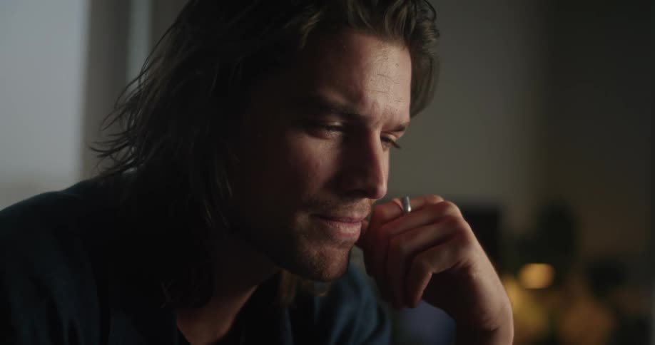 Man with long hair and black shirt smirks and types on laptop