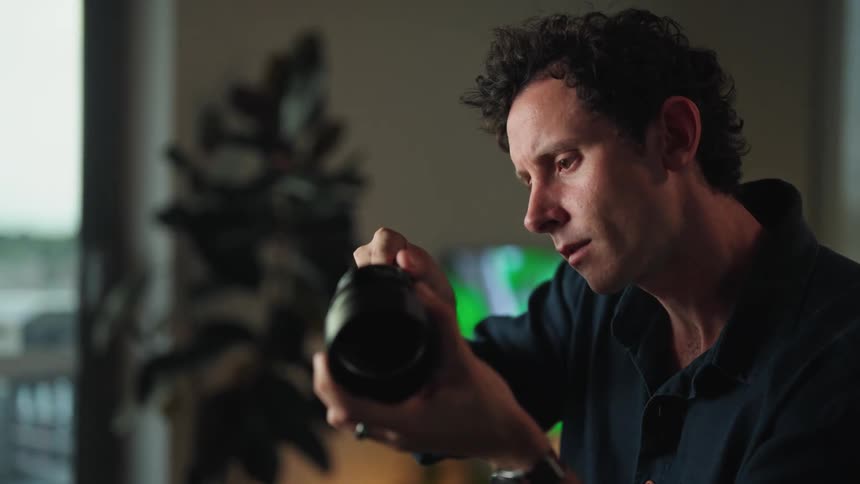 A man is holding a camera lens in his hand as he turns a screw with the other hand