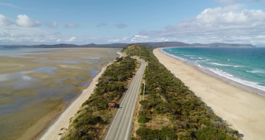 Van drives along highway through woods sandwiched between mudflats and a beach