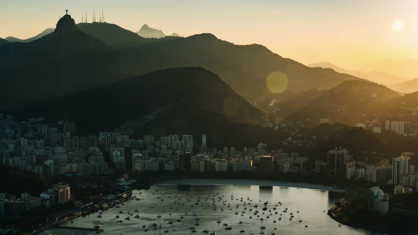 The sun shines brightly above a coastal city located at the base of a mountain range