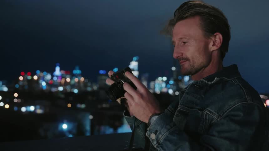 Man standing at lookout point above the city and nighttime taking photogrphs