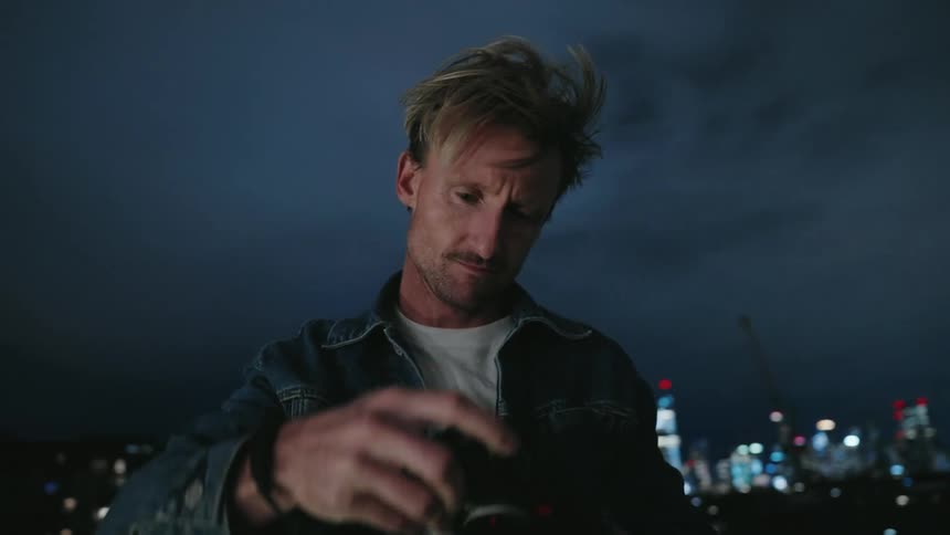 A man stands outdoors at night while taking a photography on his digital camera