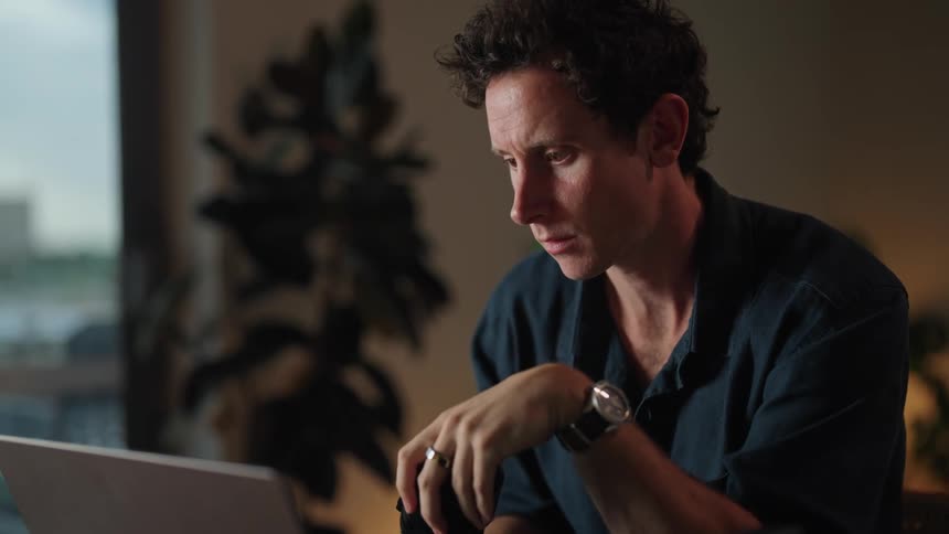 Man sitting at desk with laptop alternating typing on keyboard and handling camera lens
