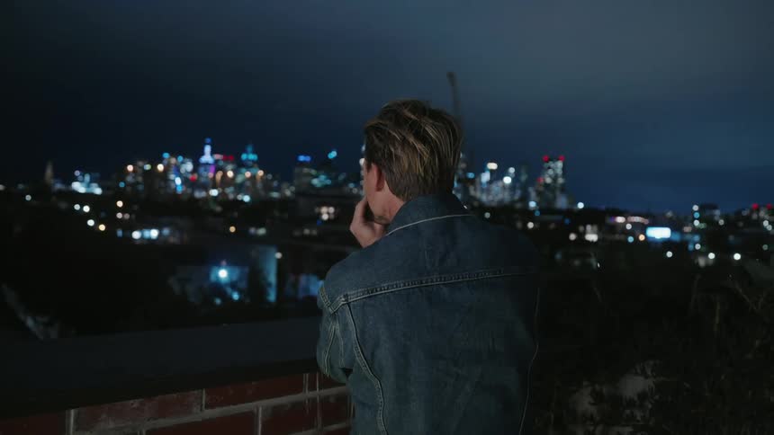 Man standing at lookout point outside photographing the nighttime city skyline